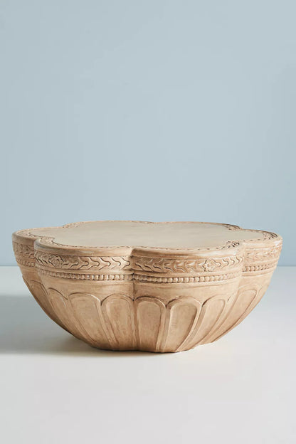 Light-toned solid wood cocktail table showing its scalloped petal-like silhouette and intricate hand-carved border
