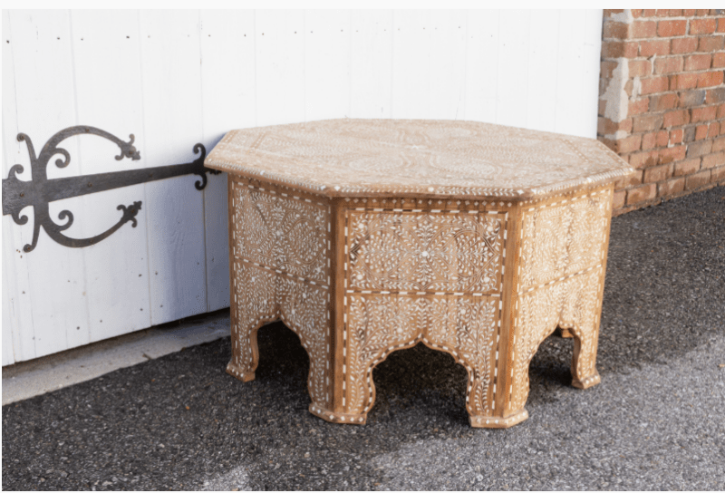 Side view of handmade octagonal bone inlay coffee table with Moorish arch base, full floral inlay coverage, and natural teak wood finish outdoors.