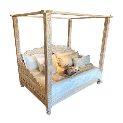 A luxury hand-carved solid wood four-poster canopy daybed with a whitewash finish, intricate vine carvings on pillars, and a scalloped frame styled with white and beige linens.