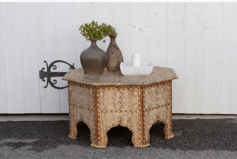 Bone inlay octagonal teak coffee table displayed outdoors with ceramic vases on top, showcasing Mandawa-style carved arch legs and floral inlay.