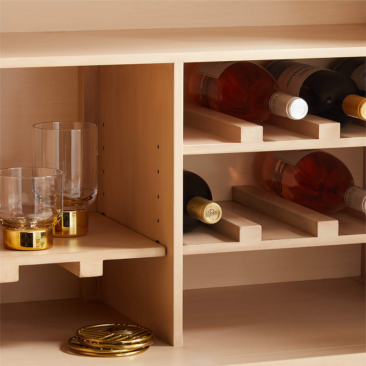Marble top wine cabinet interior close-up, showing wine bottle slots and a glass tumbler shelf with brass coasters.