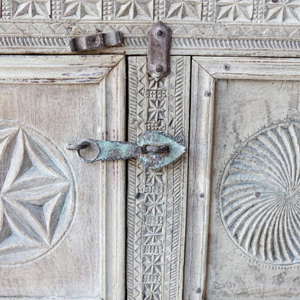 Metal-latch wooden dowry chest in a pale weathered finish, close-up of door latch between star and spiral carvings.