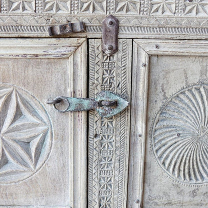 Metal-latch wooden dowry chest in a pale weathered finish, close-up of door latch between star and spiral carvings.