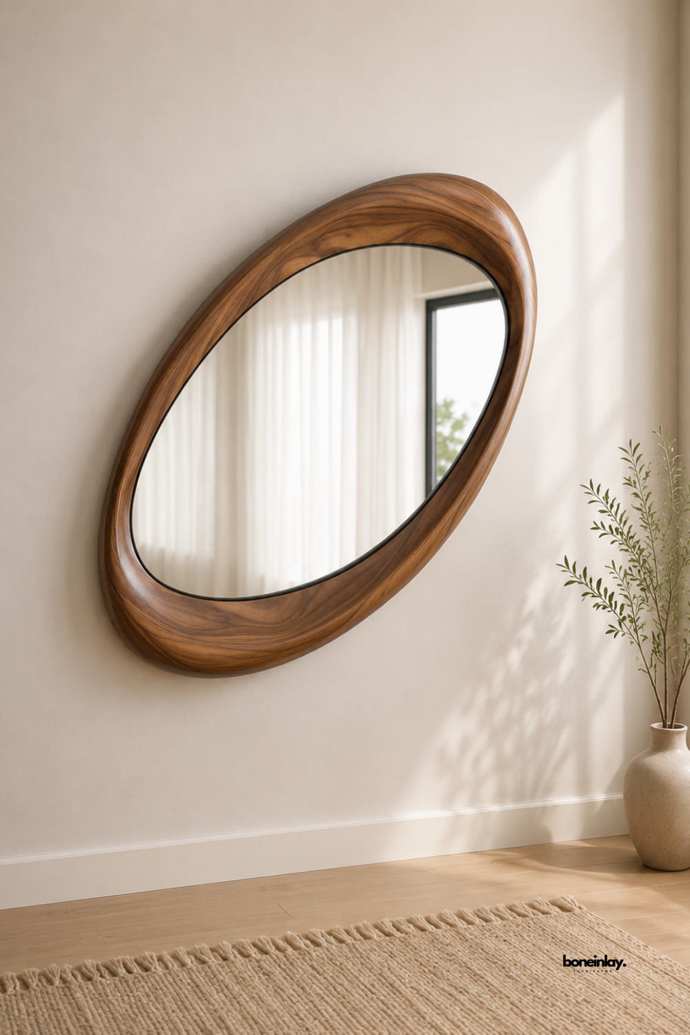 Hand-carved organic asymmetrical wooden wall mirror crafted from solid walnut with smooth, fluid pebble-inspired contours and rich natural graining. Styled in a warm minimalist room setting above light hardwood floors with a fringe jute rug, this sculptural mid-century modern mirror brings natural art and elegance to living spaces.