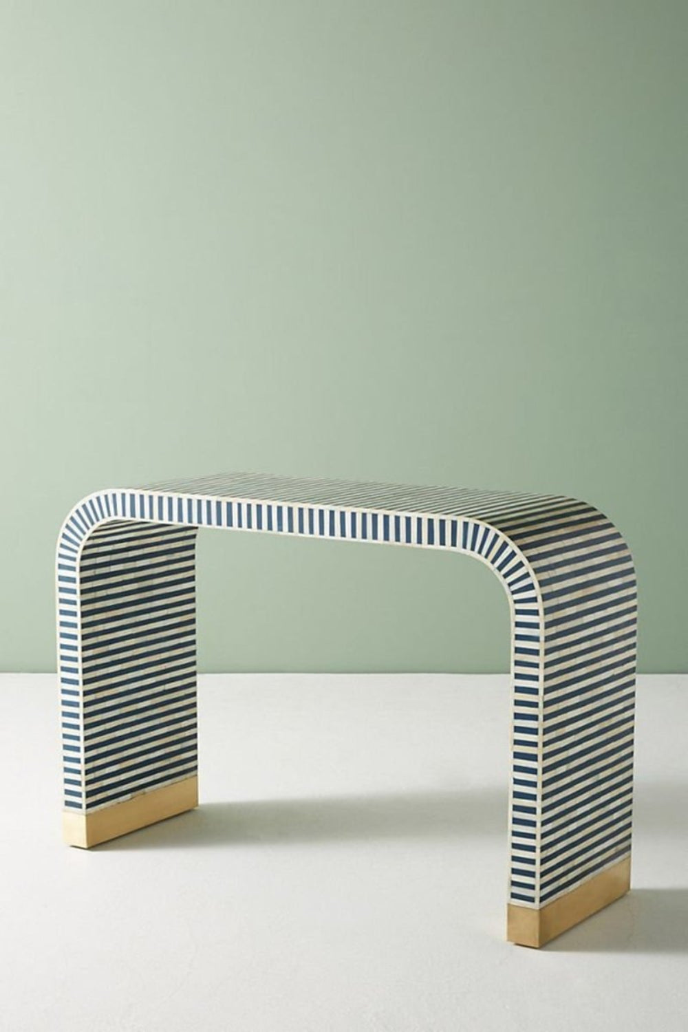 Three-quarter side angle of the blue bone inlay entryway table, showing the continuous waterfall curve, striped inlay surface, slim console profile, and brass-capped feet. the handmade table as a narrow hallway.