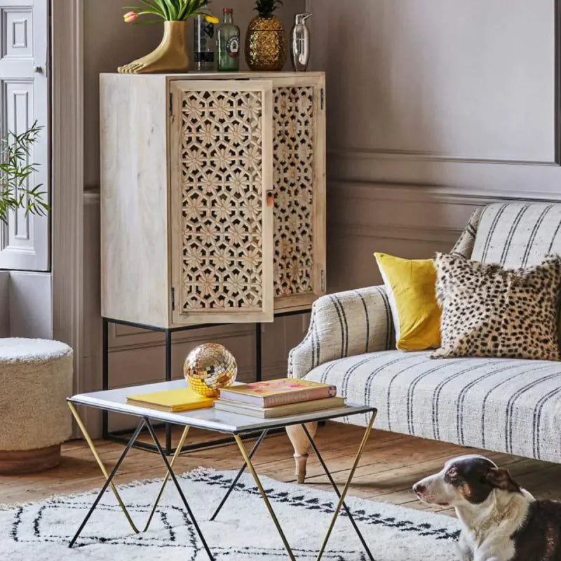 Momoka carved armoire in a white sand-washed finish, styled in a bright living room beside a beige sofa.