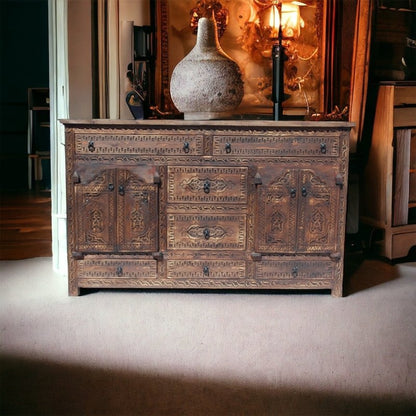 Moorish carved wood credenza in rustic timber, styled in living room beneath framed artwork with a large textured vase.
