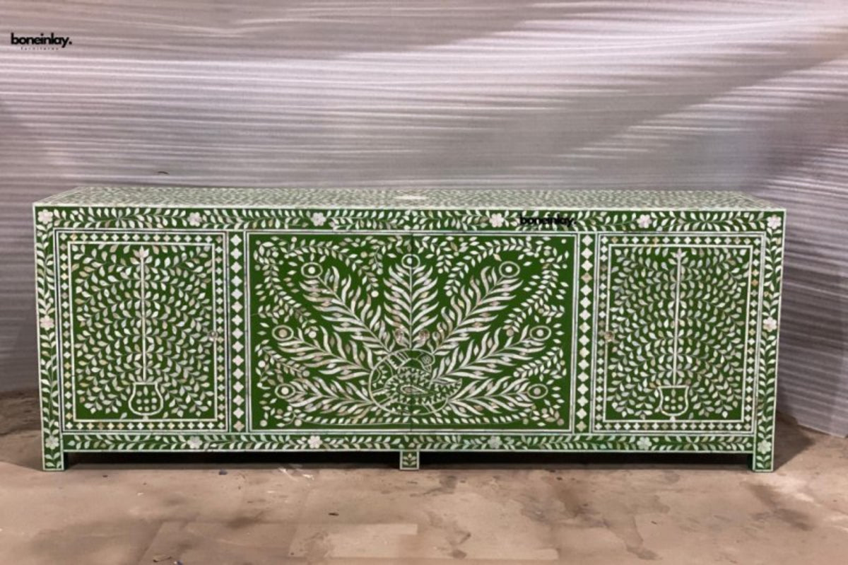 Front view of a large olive green and white mother of pearl 4-door sideboard featuring an intricate central peacock and floral tree of life pattern against a textured workshop floor.
