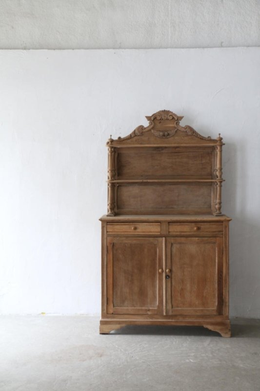 Natural finish buffet hutch with a carved top and paneled doors, distant front view against a pale wall.
