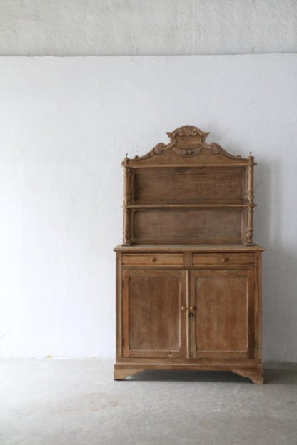 Natural finish buffet hutch with a carved top and paneled doors, distant front view against a pale wall.