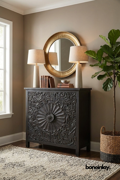 Black carved wood cabinet with a bold sunburst floral medallion design.
Detailed scroll and leaf carving radiates across both cabinet doors.
Simple block legs give it a grounded, classic silhouette.
Styled beneath a round brass mirror with matching ceramic table lamps.