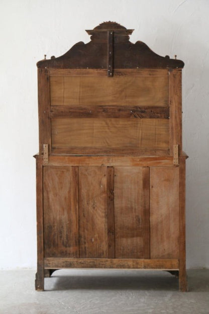 Natural wood display hutch with a shaped crown and paneled rear, back view against a light wall.