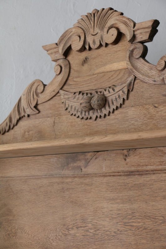 Ornate wood display cabinet with a curved carved crown, close-up of the upper trim against a pale wall.