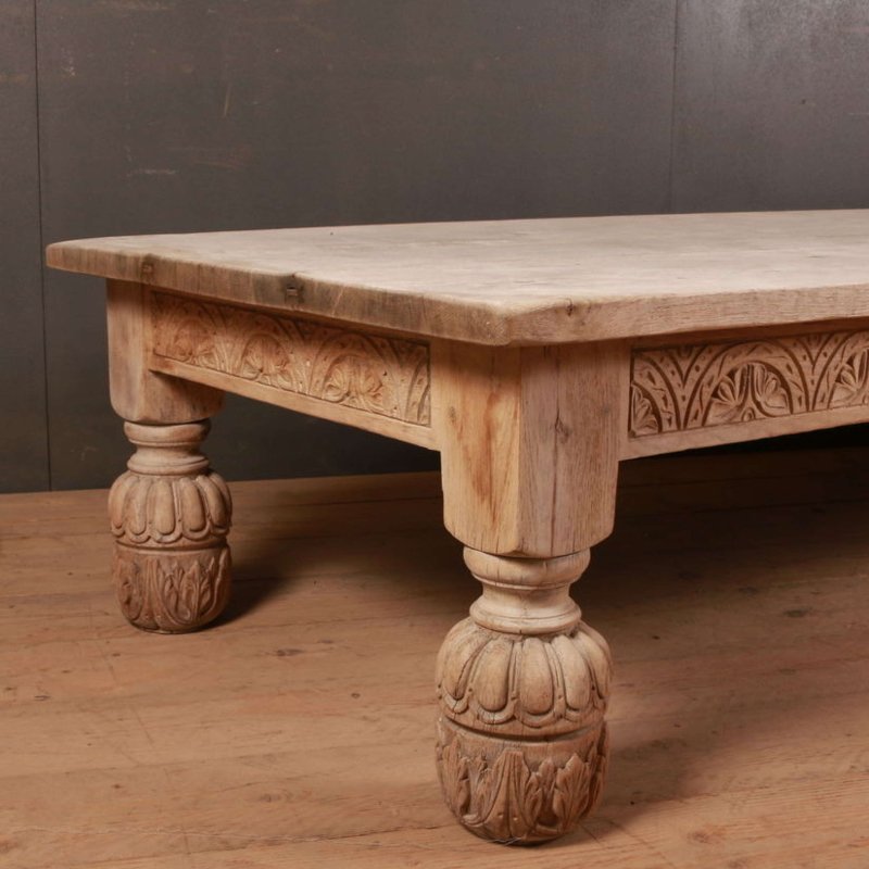 Pale wood cocktail table with a carved apron and rounded front leg, seen from an angled front view on a wood floor.