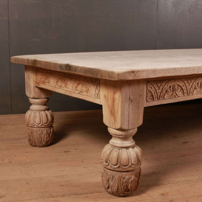 Pale wood cocktail table with a carved apron and rounded front leg, seen from an angled front view on a wood floor.