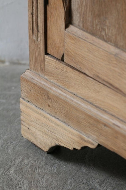 Paneled wood storage cabinet in a natural tone, angled close-up of the lower door corner and shaped base.