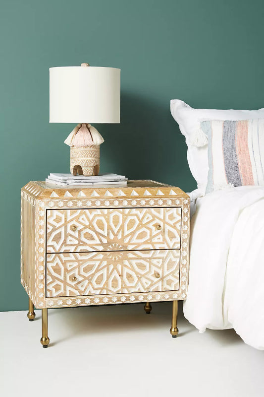 Patterned Carved Wood Night Table with brass legs, photographed from a front-right angle beside a made bed.