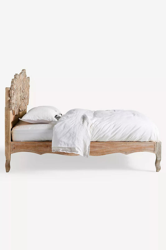 Ornate hand-carved wood bed frame with a large, intricate floral cutout headboard in a distressed whitewash finish, styled with white bedding.
