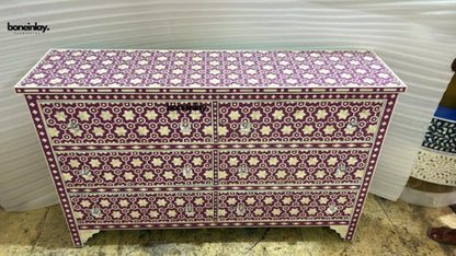 A wide plum purple and white bone inlay dresser with six drawers featuring a geometric star and floral pattern with hand-carved white knobs in a studio setting.