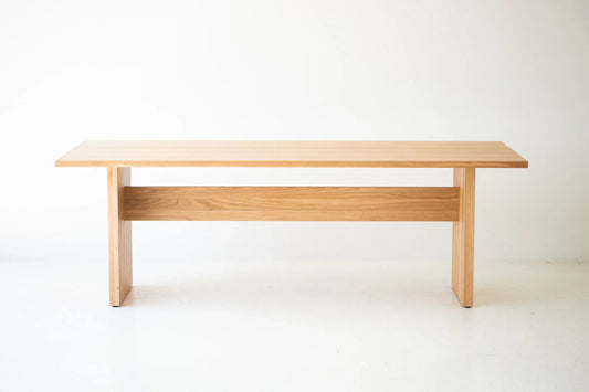 Front view of a minimalist modern solid dining table with a trestle base and natural wood grain finish against a white background.