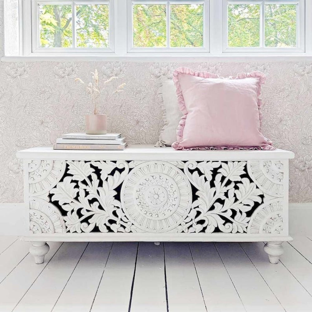 Rectangular Carved Storage Trunk in white wood, front view beneath windows with a pink cushion, books and small vase.