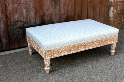 Rectangular upholstered footstool with a rustic wood frame, top view showing patterned fabric above floral carving.