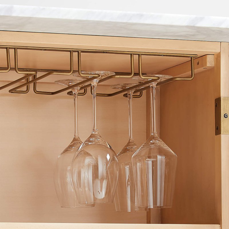 Reeded liquor cabinet interior close-up, showing four wine glasses hanging from a brass stemware rack.