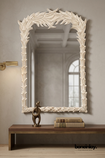 White carved wood mirror with a flowing leaf-and-feather frame design.
Oversized organic leaf carving wraps asymmetrically around the top.
Whitewashed finish gives it a soft, sculptural, botanical look.
Styled above a walnut bench with a bronze figurine and stacked books.