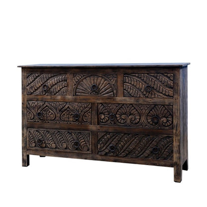 Seven-drawer wood chest of drawers featuring carved fronts and metal ring pulls against a dark finish.