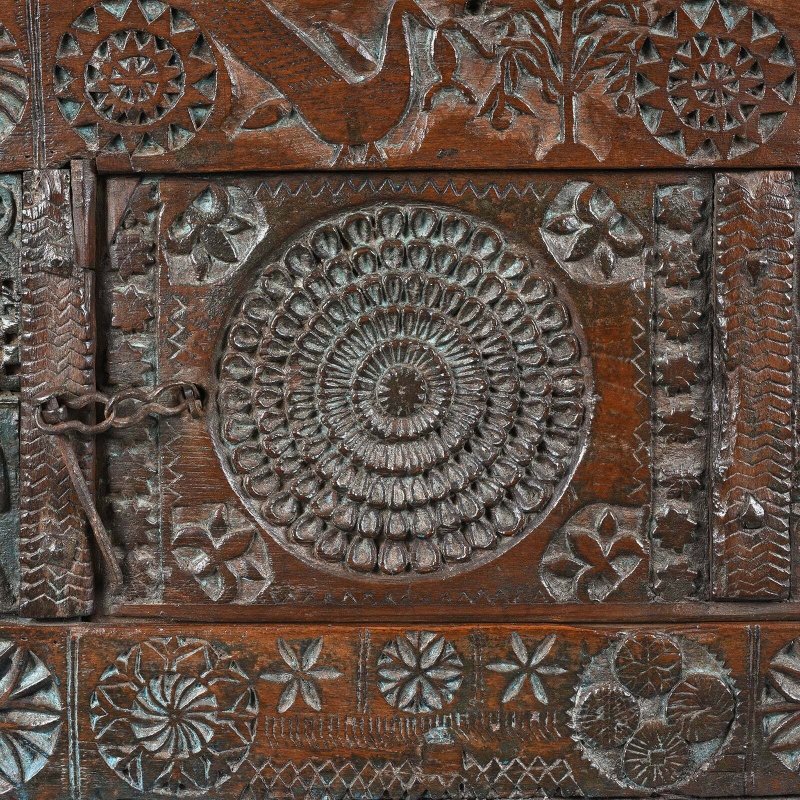 Rosette panel dowry chest in natural walnut wood, front view close-up of the circular carving and metal door latch.