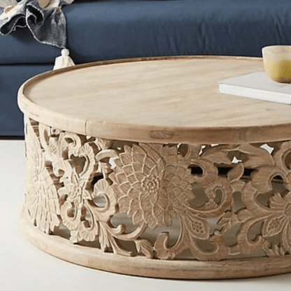 Round fretwork coffee table in natural solid wood, base detail view showing carved flowers beneath the rim.