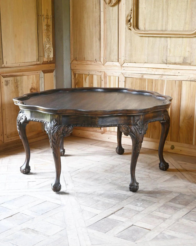 Round wood cocktail table in a front view, showing its dark tabletop, shaped apron and four curved legs.