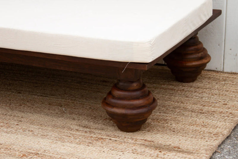 Lounge daybed with a rounded dark wood foot, shown in a close-up of the leg beneath the white cushion.