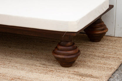 Lounge daybed with a rounded dark wood foot, shown in a close-up of the leg beneath the white cushion.