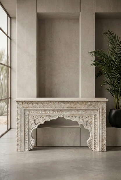 Rustic carved console table in wood, styled in entryway beside a tall window and potted palm, with a scalloped arch.