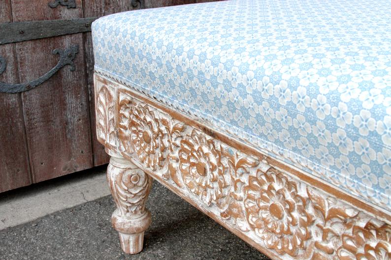 Rustic carved upholstered seat in solid wood, edge detail view showing floral relief beneath patterned fabric piping.