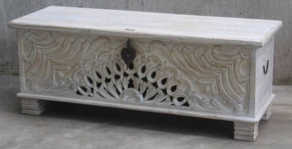 Rustic carved wooden trunk in solid wood, front view showing a dark right side handle and peacock carving above block feet.