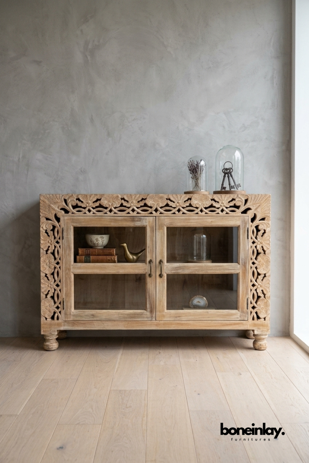Whitewashed carved wood cabinet with glass-front display doors.
Ornate floral lattice carving frames the top and side edges.
Two glass doors reveal open shelving for books and decor.
Raised on turned bun feet for a classic vintage look.