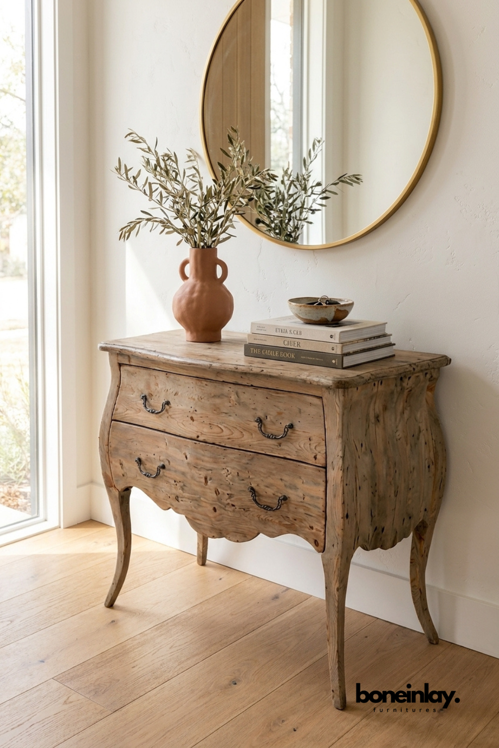 Rustic curved wood dresser styled beneath a round mirror with decorative books and a terracotta vase, creating a cozy farmhouse-inspired interior.