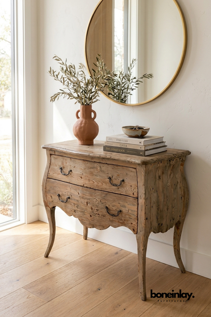 Rustic curved wood dresser styled beneath a round mirror with decorative books and a terracotta vase, creating a cozy farmhouse-inspired interior.