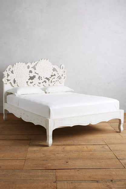 Rustic lotus-carved headboard bed in natural mango wood, styled with white pillows against a soft teal bedroom wall.