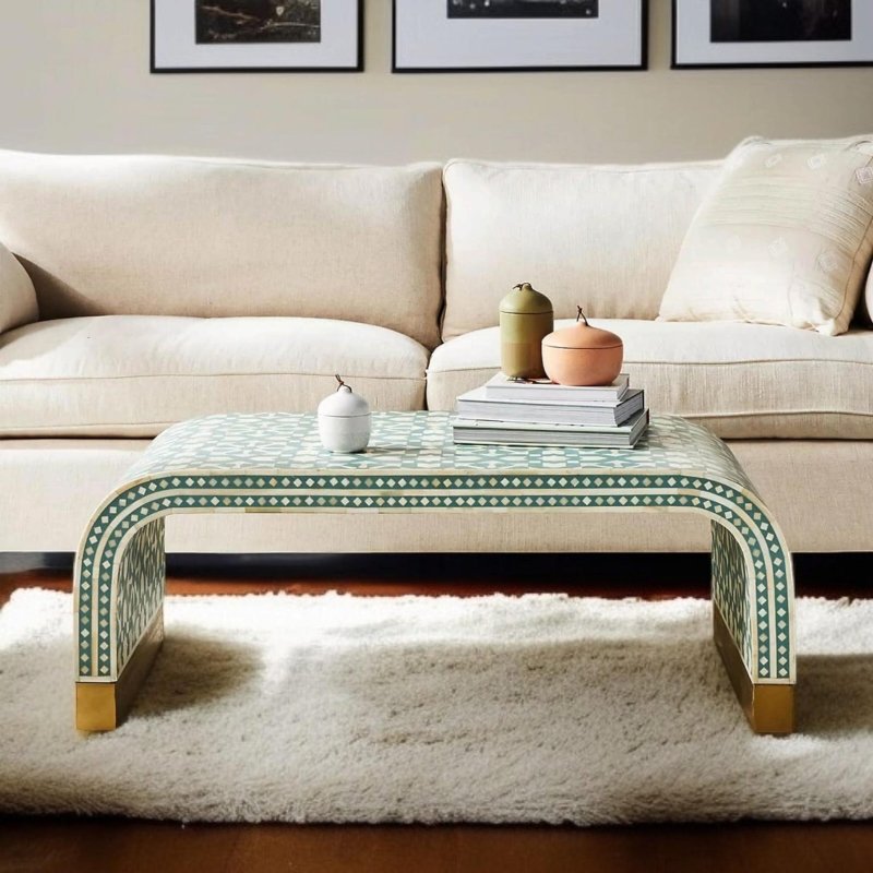 Handcrafted sage green and white diamond-pattern bone inlay waterfall center table with rounded curved edges and gold brass feet, styled with decorative objects on a cream sofa background