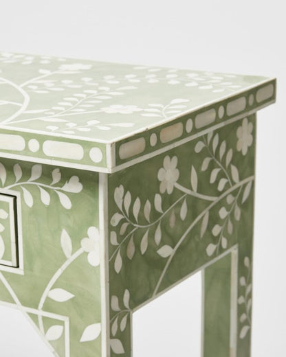 Corner detail of a sage green mango wood bone inlay console table showing geometric border inlay along the tabletop edge and floral vine pattern on the apron