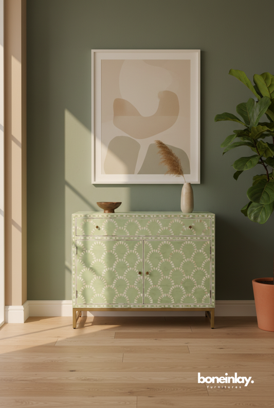 Sage green bone inlay scalloped fish-scale cabinet with one drawer and two doors, styled in a sunlit living room with abstract wall art and indoor plants