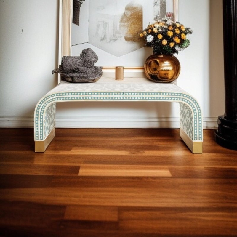 Sage green and white bone inlay waterfall table used as an entryway console, topped with decorative sculpture and floral arrangement in bronze vase on warm wooden flooring
