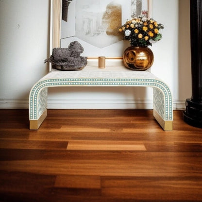 Sage green and white bone inlay waterfall table used as an entryway console, topped with decorative sculpture and floral arrangement in bronze vase on warm wooden flooring