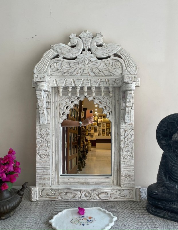 Scalloped Arch Wall Mirror in rustic carved wood, front view with a floral dish below and a dark statue to the right.