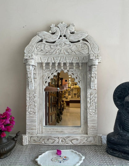 Scalloped Arch Wall Mirror in rustic carved wood, front view with a floral dish below and a dark statue to the right.