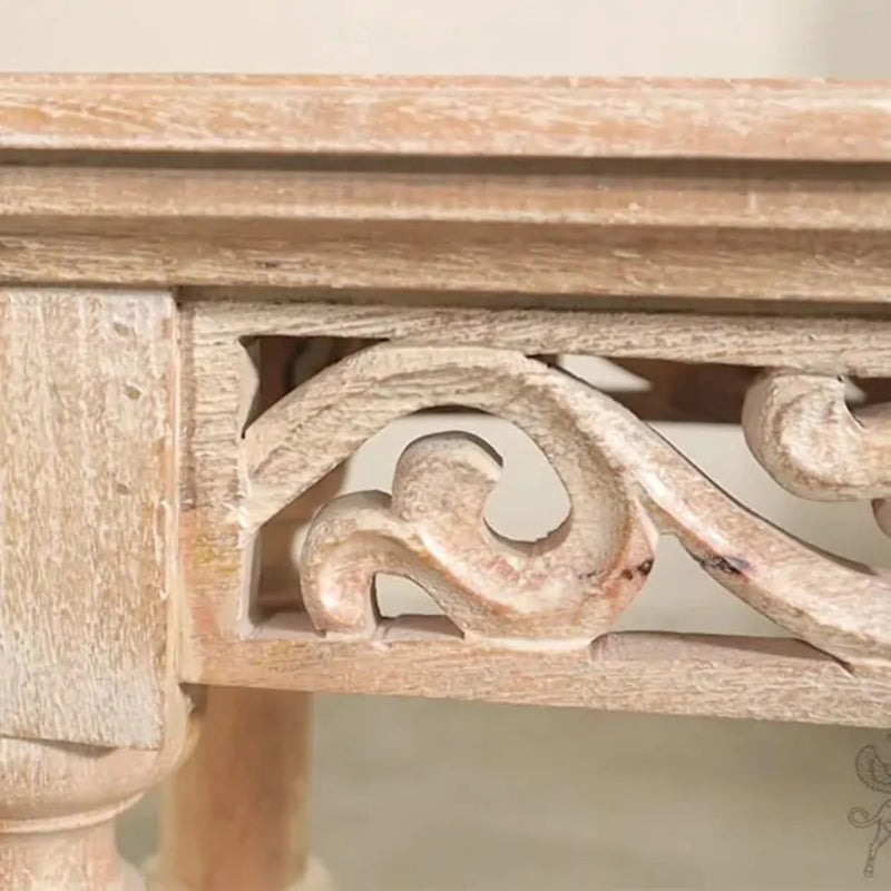 Scrollwork foyer table with carved wood trim in a light natural finish, macro view of the front apron on neutral background.