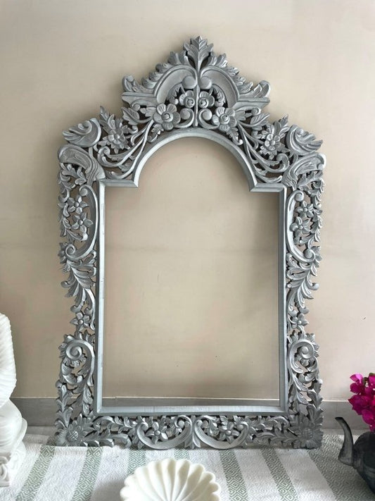 Silver arched mirror frame in solid wood, front view showing an empty center surrounded by floral scrollwork.